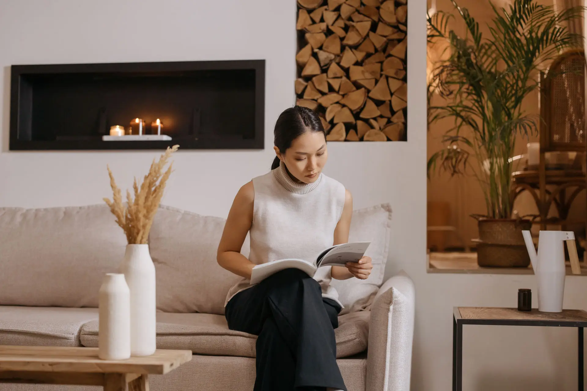 A woman reading sitting a living room with a open fire behind her , wood logs , power of scent , scent, interior design blog